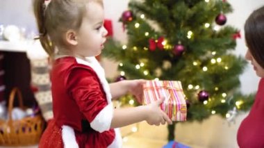 Bebek ve hamile bir anne Noel ağacına kırmızı top oyuncağı asıyor. Mutlu çocukluk kavramı. Çocuk ve anne Noel toplarıyla ağacı süslerler. Küçük çocuk ve bir ebeveyn Noel ağacının yanında oynuyorlar..