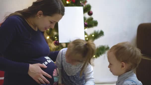 Двое детей ощупывают, слушают и целуют живот беременной матери. — стоковое видео