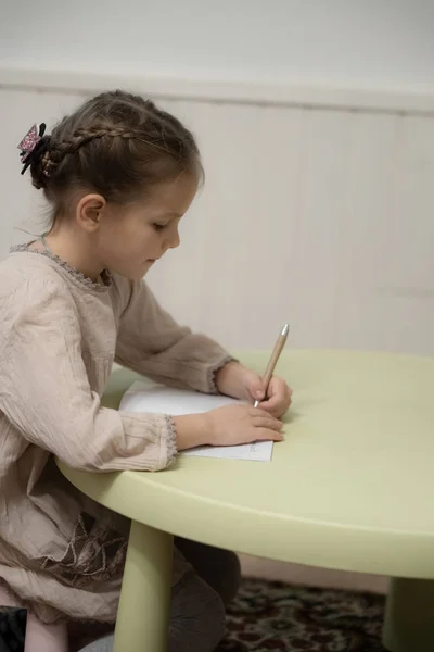 Een donker blond meisje in een beige jurk doet huiswerk — Stockfoto