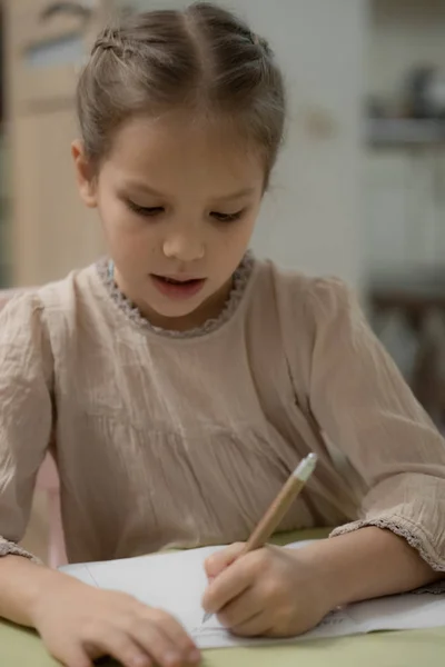 Une fille blonde foncée dans une robe beige fait ses devoirs — Photo