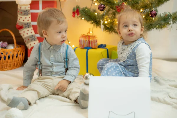 Dziewczyna i chłopiec siedzieć przed choinką i kominkiem w pobliżu białego arkusza papieru — Zdjęcie stockowe