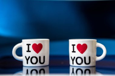 Kırmızı kalpli iki beyaz bardak ve klasik mavi arka planda seni seviyorum.