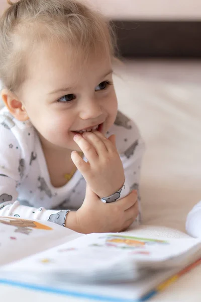 Niños encantadores - hermano y hermana, leyendo un libro, en la cama. Primer plano de los niños en la cama leyendo un libro. Un niño y una niña de blanco están jugando en la cama. Bebés de blanco en la cama. Lindos niños . — Foto de Stock