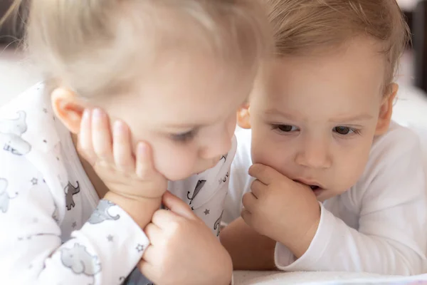 Beaux enfants - frère et sœur, lisant un livre, sur le lit. Gros plan d'enfants au lit lisant un livre. Un garçon et une fille en blanc jouent sur le lit. Des bébés en blanc sur le lit. Enfants mignons. — Photo