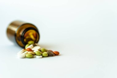 İlaç ve haplar. Beyaz arka planda, çok renkli ilaçlar var. Kahverengi cam şişe ve beyaz arka planda haplar. Ters çevrilmiş bir kavanozun üzerine dökülen çok renkli tabletler.