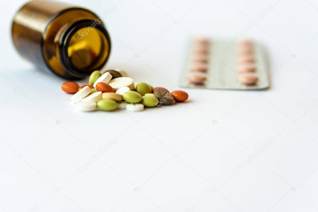 Medicine and pills. Multi-colored medicines on a white background close-up. Brown glass bucket and plate with pills on a white background. Multi-colored tablets that spilled from an inverted jar onto