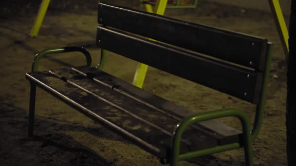 Swing on the playground at night, no one in the park. Close-up rides in the dark. The swing sways slowly. Deserted playground at night. Gloomy night scenery in the park. — Stock Video