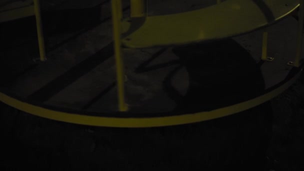 The carousel spins at night on a playground in a deserted park. Rides in the dark. Close-up of a swing in a gloomy park. Deserted playground at night. Swing swing slowly. — Stock Video