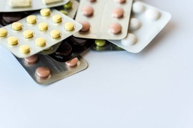 İlaç ve haplar. Beyaz arka planda, çok renkli ilaçlar var. Beyaz arka planda çok renkli tabletlerle kaplanmış. Ters çevrilmiş bir kavanozdan beyaz bir kavanoza dökülen çok renkli haplar.