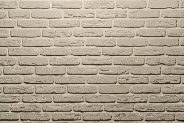White brick wall of a warm shade lit from above by a lamp. White brick wall, perfect as a background, square photograph. The brick background is white with a warm shade.
