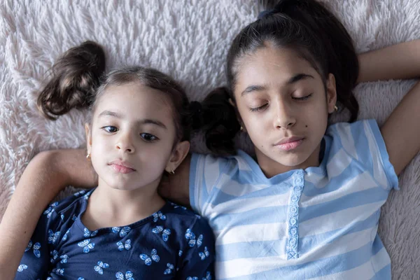 两个中东年轻可爱的女孩，姐妹们，躺在床上，在阳光下看着智能手机。躺在床上拿着电话的波斯女孩中东儿童. — 图库照片