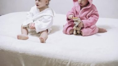 Banyo yaptıktan sonra ıslak saçlı, beyaz arka planda iki çocuk. Beyaz bir yatakta duştan sonra kız ve erkek. Bornozlu kız ve erkek kardeşler yatmadan önce oynarlar. Çocuklar, İrlandalı ikizler
