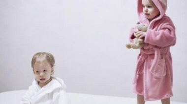 Banyo yaptıktan sonra ıslak saçlı, beyaz arka planda iki çocuk. Beyaz bir yatakta duştan sonra kız ve erkek. Bornozlu kız ve erkek kardeşler yatmadan önce oynarlar. Çocuklar, İrlandalı ikizler