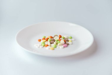 Beyaz tabakta haplar. Beyaz arka planda çok renkli haplar. Beyaz bir masada ilaç. Tabaktaki yemek kisvesi altında haplar. Yiyeceği sembolize eden küçük bir yığın..