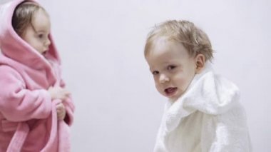 Banyo yaptıktan sonra ıslak saçlı, beyaz arka planda iki çocuk. Beyaz bir yatakta duştan sonra kız ve erkek. Bornozlu kız ve erkek kardeşler yatmadan önce oynarlar. Çocuklar, İrlandalı ikizler