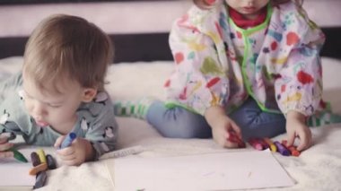 Yatakta kremalı iki şirin çocuk çiziyor. Kız ve oğlan kalemlerle yatakta oynuyorlar. Erkek ve kız kardeş ikizler karınlarının üstünde yatarken kalemle çizerler..