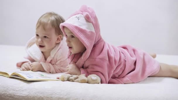 Two kids in bathrobes on a white background with wet hair after taking a bath. Boy and girl after shower on a white bed. Brother and sister in bathrobes play before bedtime. Children Irish twins on a — Stock Video