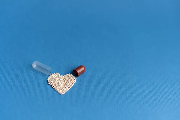 Granules poured from a heart-shaped capsule on a classic blue background. Heart shaped medicines. Heart symbol drawn by pills. — Stock Photo, Image