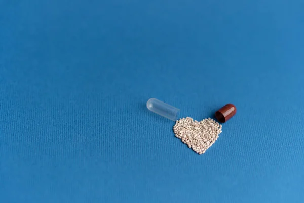 Granules poured from a heart-shaped capsule on a classic blue background. Heart shaped medicines. Heart symbol drawn by pills. — Stock Photo, Image