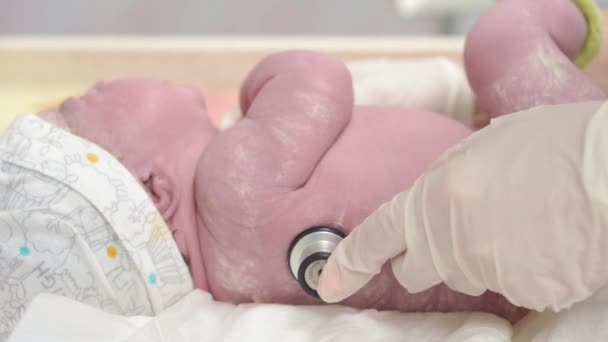 Närbild porträtt av ett nyfött barn i ett ursprungligt smörjmedel vars kvinnliga händer i medicinska handskar undersöka ett stetoskop. Barnet nyfött efter födseln gråter första minuterna av livet. — Stockvideo