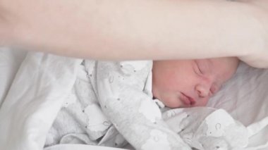 Kadın eller, beyaz arka planda yeni doğmuş bir bebeğe şapka takıyor. Annem yeni doğan bebeğine şapka takıyor. Hayatın ilk dakikalarında yeni doğmuş bir bebek..