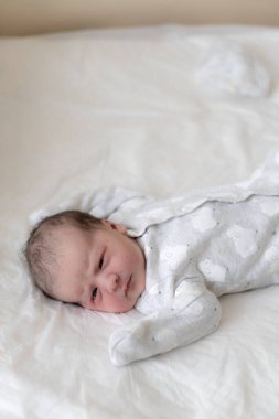 Yeni doğmuş bir bebek, hayatının ilk dakikalarında gözleri açık sırt üstü yatar. İlkel yağ izleri taşıyan yeni doğmuş bir bebek gözlerini kamaştırıyor. Bebek şaşı görünüyor..