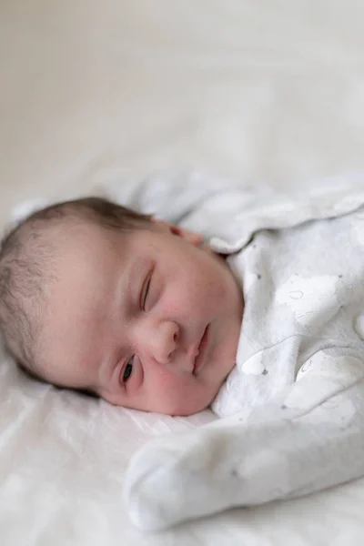 新生儿仰卧在床上，在生命的最初几分钟睁开眼睛。一个有原始油脂痕迹的新生儿斜视着眼睛. — 图库照片