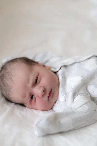 新生儿仰卧在床上，在生命的最初几分钟睁开眼睛。一个有原始油脂痕迹的新生儿斜视着眼睛. — 图库照片