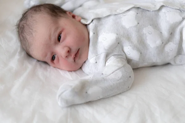 Ένα νεογέννητο μωρό βρίσκεται στην πλάτη του με ανοιχτά μάτια στα πρώτα λεπτά της ζωής. Ένα νεογέννητο με ίχνη αρχέγονου λίπους τρίβει τα μάτια του. Το μωρό κοιτάζει αλληθωρίζοντας. — Φωτογραφία Αρχείου