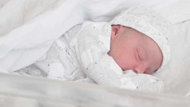 Em um close-up, um bebê recém-nascido em uma cama de vidro médico para recém-nascidos nos primeiros dias de vida acorda e abre os olhos. Um bebê recém-nascido sorri através de um sonho. Bebê recém-nascido nos primeiros minutos de — Vídeo de Stock