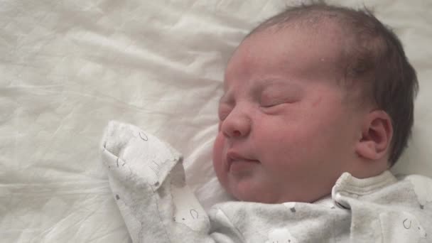 Közelkép egy újszülött arcáról a korai napokban, aki felébred és kinyitja a szemét. Egy újszülött grimaszol egy álomban. Újszülött az élet első perceiben. — Stock videók