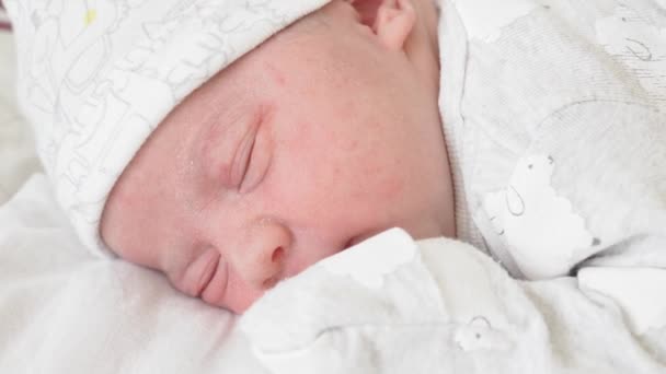 Primer plano de la cara de un bebé recién nacido en los primeros días que se despierta y abre los ojos. Un bebé recién nacido hace muecas a través de un sueño. Recién nacido en los primeros minutos de vida . — Vídeo de stock