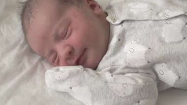 İlk günlerde gülümseyen ve gözlerini açan yeni doğmuş bir bebeğin yüzünü kapatın. Yeni doğmuş bir bebek bir rüyada yüzünü buruşturur. Hayatın ilk dakikalarında yenidoğan.