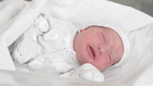 En el plan firme, un bebé recién nacido en una cama de vidrio médico para recién nacidos se despierta y hace muecas en los primeros días de vida. Un bebé recién nacido hace muecas a través de un sueño. Recién nacido en los primeros minutos de vida — Vídeos de Stock