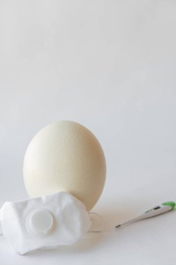 Solunum cihazında büyük bir paskalya devekuşu yumurtası ve bir termometre. Yumurta, solunum cihazı ve termometre. Paskalya ve Coronavirus, Covid-19. Devekuşu yumurtası, tıbbi maske ve beyaz arka planda termometre..