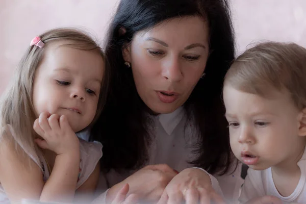 Grand-mère avec petit-fils et petite-fille au lit lisant un livre. Grand-mère avec petits-enfants au lit pendant l'enseignement à distance. Grand-mère joue avec ses petits-enfants au lit pendant la quarantaine . — Photo