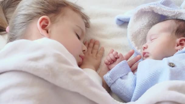 Close-up bebê recém-nascido e menina dormindo. Um recém-nascido com uma criança em roupas azuis em um fundo bege é sagrado face a face. Duas irmãs dormem à tarde na cama cara a cara . — Vídeo de Stock