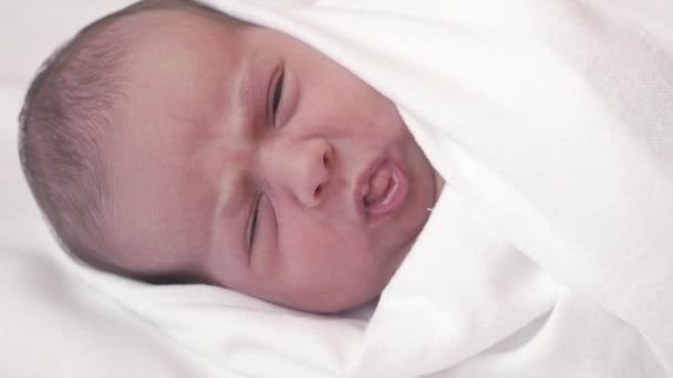 Close-up van een pasgeboren baby lachend in een witte luier. Close-up baby op een witte achtergrond ontwaakt, lacht, grimmig, opent zijn ogen. — Stockvideo