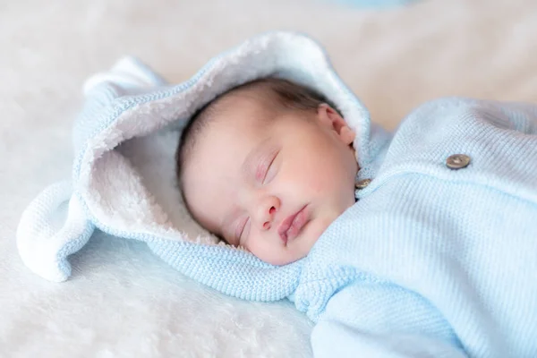 Um bebé recém-nascido de perto. Vista lateral de um bebê recém-nascido dormindo profundamente de costas em uma blusa azul com um capuz e orelhas em um fundo branco. Retrato de um bebê recém-nascido adormecido em um fundo bege . — Fotografia de Stock