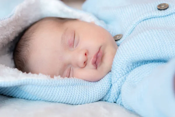 新生儿的特写。一个新生婴儿穿着蓝色上衣，头罩和耳朵，白色背景，仰卧在床上熟睡的侧视图。米色背景下睡着的新生儿的肖像. — 图库照片