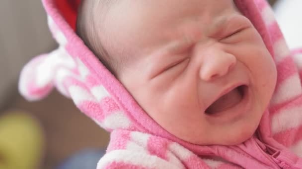 El bebé recién nacido estornuda de cerca. Rostro cerrado de un bebé estornudando. Mamá sostiene a un niño en sus brazos, lo que estornuda. Retrato cercano de un niño estornudando. El niño está despierto en los brazos de sus madres en una blusa rosa — Vídeos de Stock