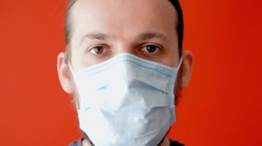Coronavirus, salgın, salgın, karantina, kendini izole etme, güvenlik, koruma, tıp konsepti - uzun saçlı, sakallı, tıbbi koruyucu maskeli, sade kırmızı arka planda genç adam..