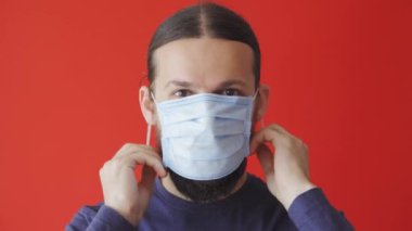 Covid-19, salgın, salgın, karantina, kendini izole etme, koruma, ilaç konsepti - mavi koruyucu maske takan uzun saçlı adamın portresi kırmızı arka planda, kopyalama spazmı.