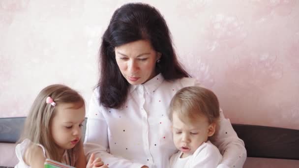 Famille, enfance, maternité, parentalité, auto-isolement, concept d'enseignement à distance Grand-mère et petits-enfants garçon fille lit livre sur le lit. Femme âgée, enfants. Nounou aînée, les enfants jouent à la maison. — Video