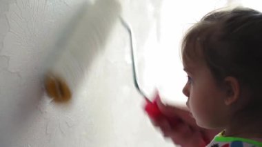 Onarım, yenileme, ev, aile, çocukluk, ebeveynlik, babalık, kendini izole etme, karantina konsepti - patenle oynayan 3 yaşında küçük bir kız, apartman duvarını beyaz boyayla boyuyor..