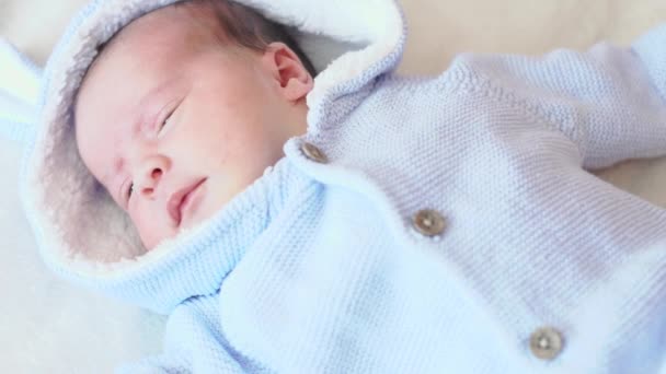 Infância, infância, cuidado, conceito de crianças - close up retrato de um bebê recém-nascido acordado deitado de costas em uma blusa azul com um capuz em um fundo bege na cama, vista superior — Vídeo de Stock