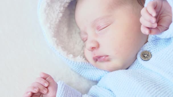 Baby, kindertijd, verzorging, kinderen concept - close-up portret van een pasgeboren baby slapen wakker liggen op zijn rug in een blauwe blouse met een kap op een beige achtergrond op het bed, bovenaanzicht. — Stockvideo