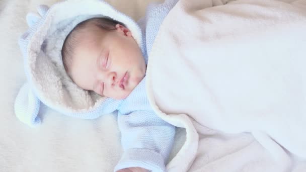 Infancia, infancia, cuidado, concepto de niños - retrato de cerca de un bebé recién nacido durmiendo despertando acostado boca arriba en una blusa azul con una capucha sobre un fondo beige en la cama, vista superior . — Vídeos de Stock