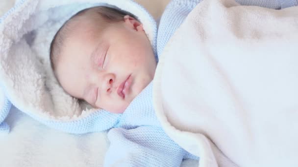 Infancia, infancia, cuidado, concepto de niños - retrato de cerca de un bebé recién nacido durmiendo despertando acostado boca arriba en una blusa azul con una capucha sobre un fondo beige en la cama, vista superior . — Vídeos de Stock