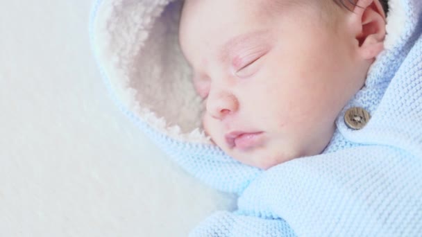 Infancia, infancia, cuidado, concepto de niños - retrato de cerca de un bebé recién nacido durmiendo despertando acostado boca arriba en una blusa azul con una capucha sobre un fondo beige en la cama, vista superior . — Vídeo de stock
